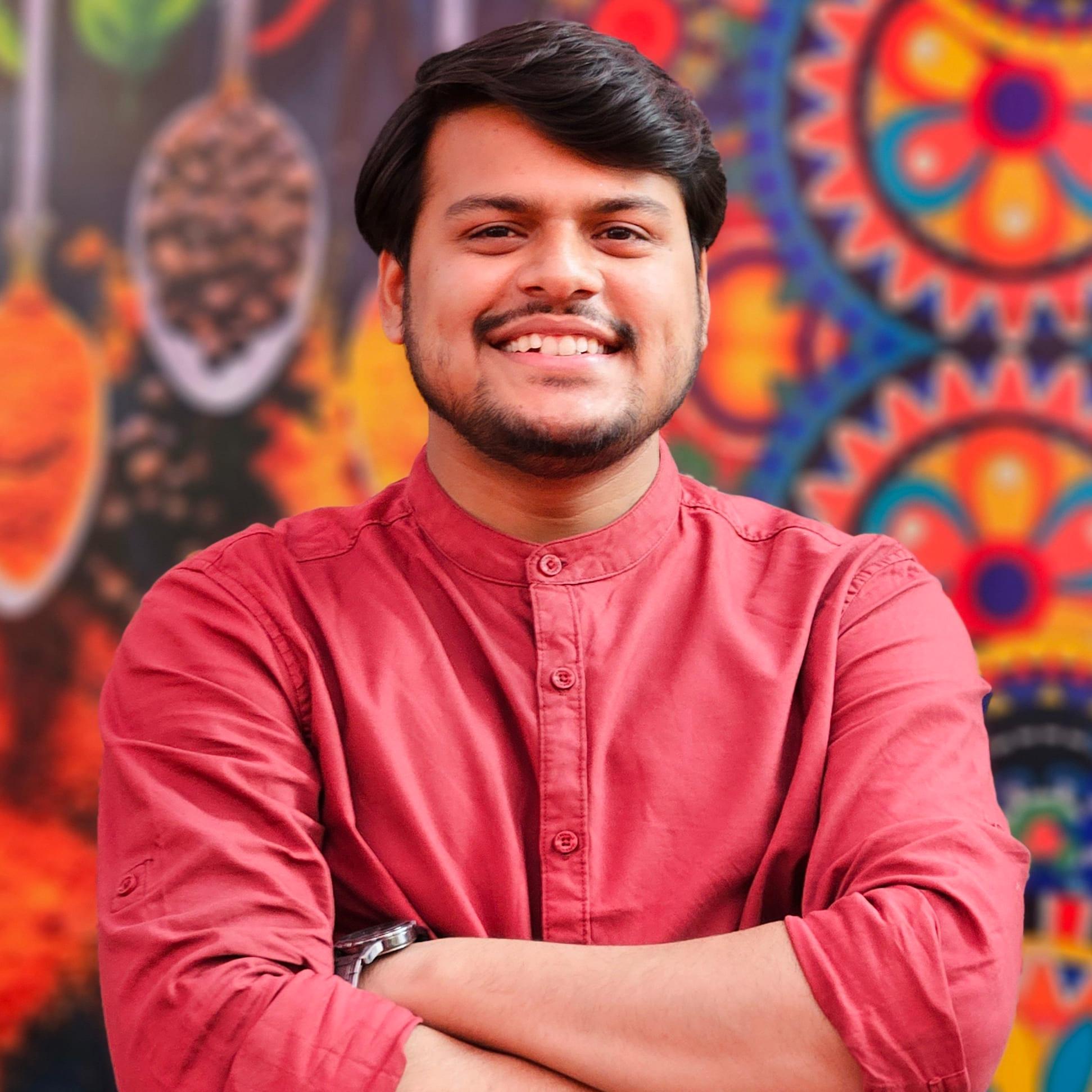 Shubham Nagota, smiling, arms crossed, in a red shirt in front of a colourful mural